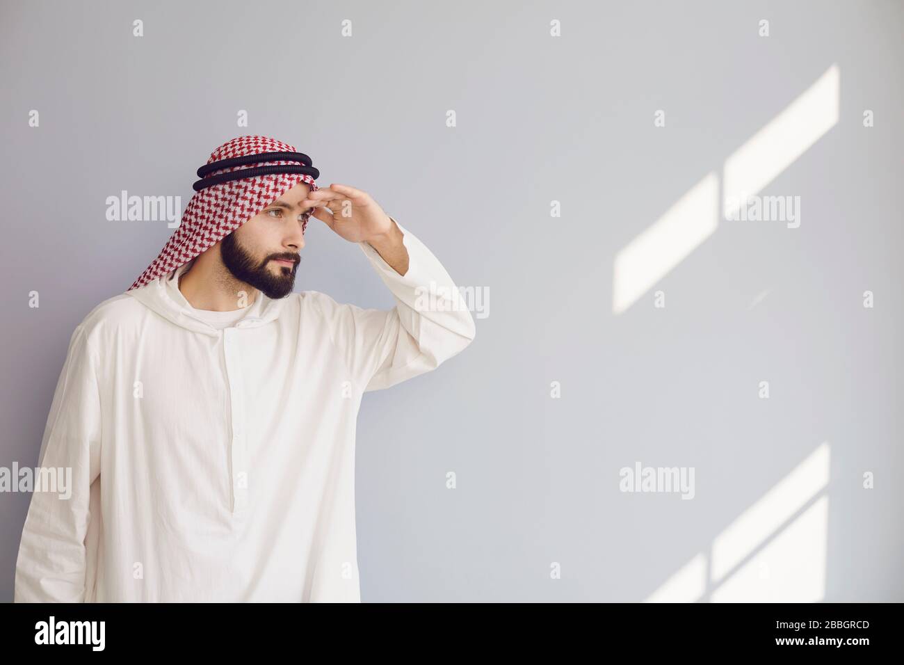 Attraktiver lächelnder arabischer Mann, der auf einem grauen Hintergrund nach Text blickt. Stockfoto