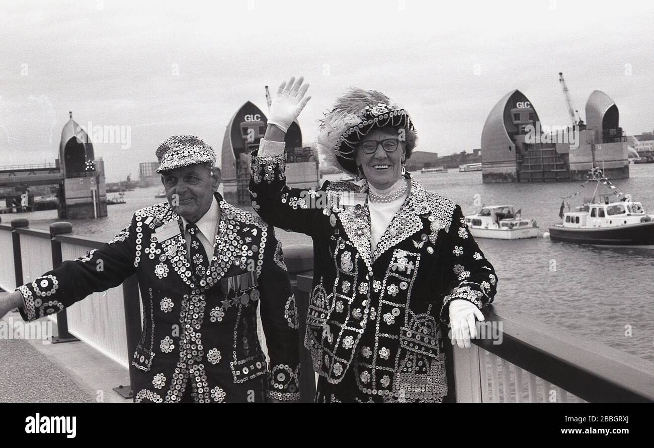 1984 tragen Londons Perlkönig und Königin ihre traditionellen Outfits. Jacken mit Perlmuttknöpfen, die zusammen an den Royal Docks stehen, bei der Eröffnung der neuen Thames Barrier, South London, England, Großbritannien durch Königin Elizabeth II..stellvertretend für Londons Arbeiterkultur, "Pearlies", wie sie auch bekannt sind, Entstanden aus den Coster Kings und Queens, die als Führer der Londoner Straßenhändler gewählt wurden. Stockfoto