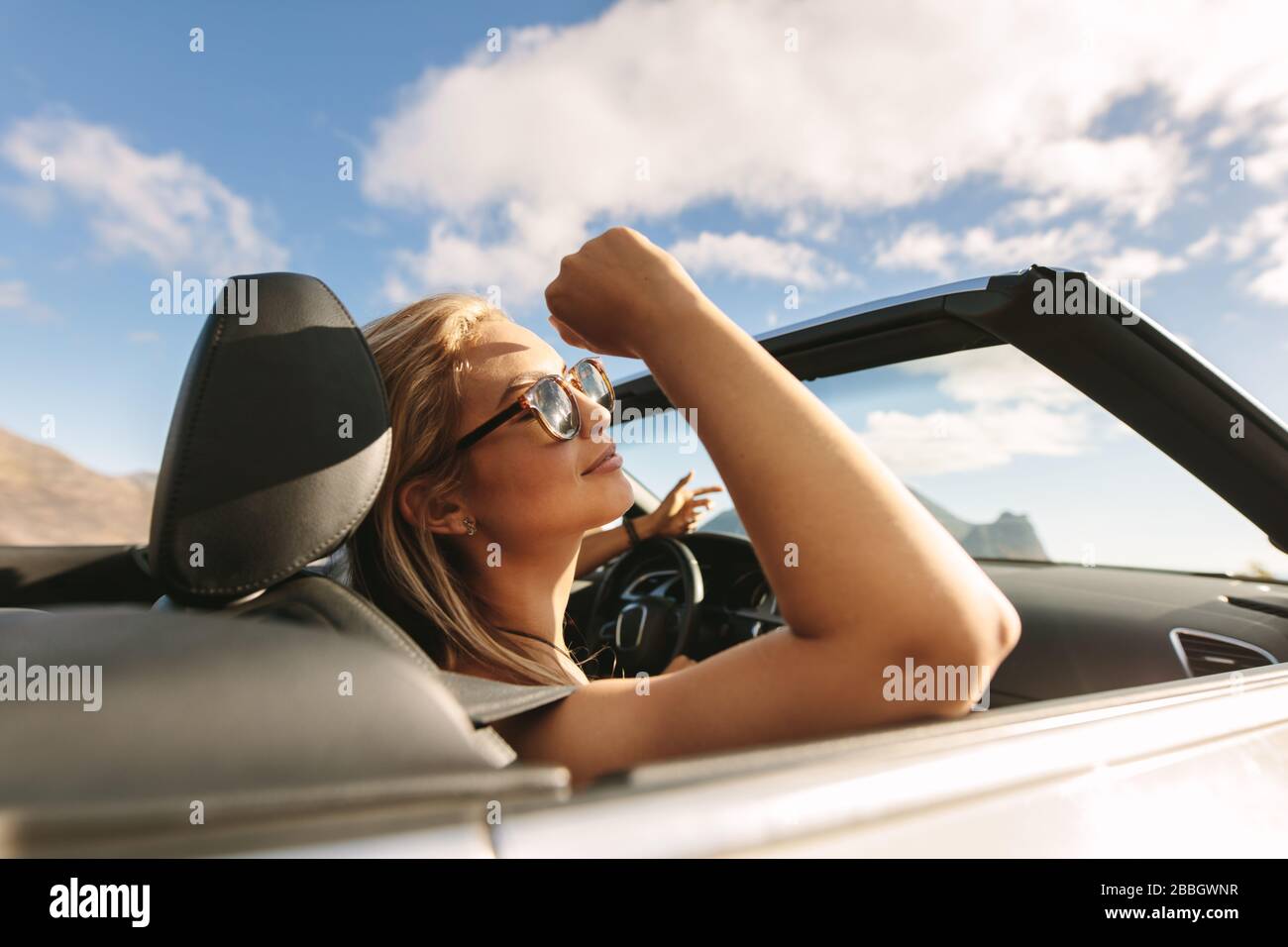 Attraktive Frau mit Sonnenbrille, die in einem Cabrio-Auto unterwegs ist. Frau auf einer Autofahrt. Stockfoto