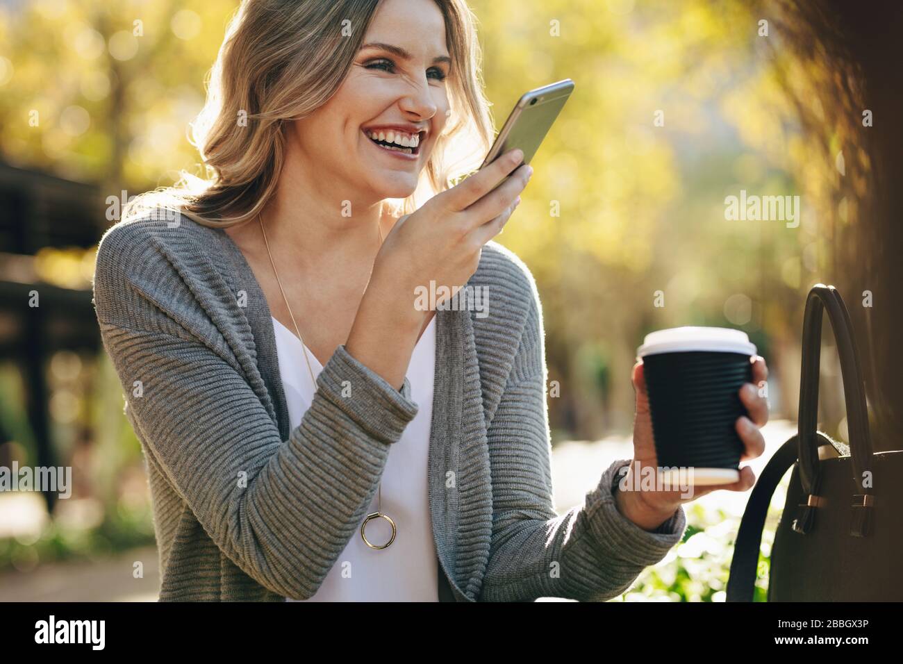 Frau, die draußen sitzt und telefoniert. Frau mit Kaffee und Telefonanruf außerhalb der Stadt. Stockfoto