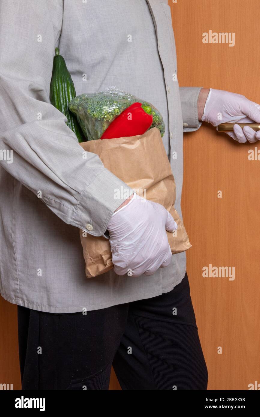 Ein Mann, der medizinische Handschuhe und eine Einkaufstasche mit frischem Gemüse trägt, betritt das Haus. Konzept der Stärkung des Immunsystems und des Schutzes Agai Stockfoto