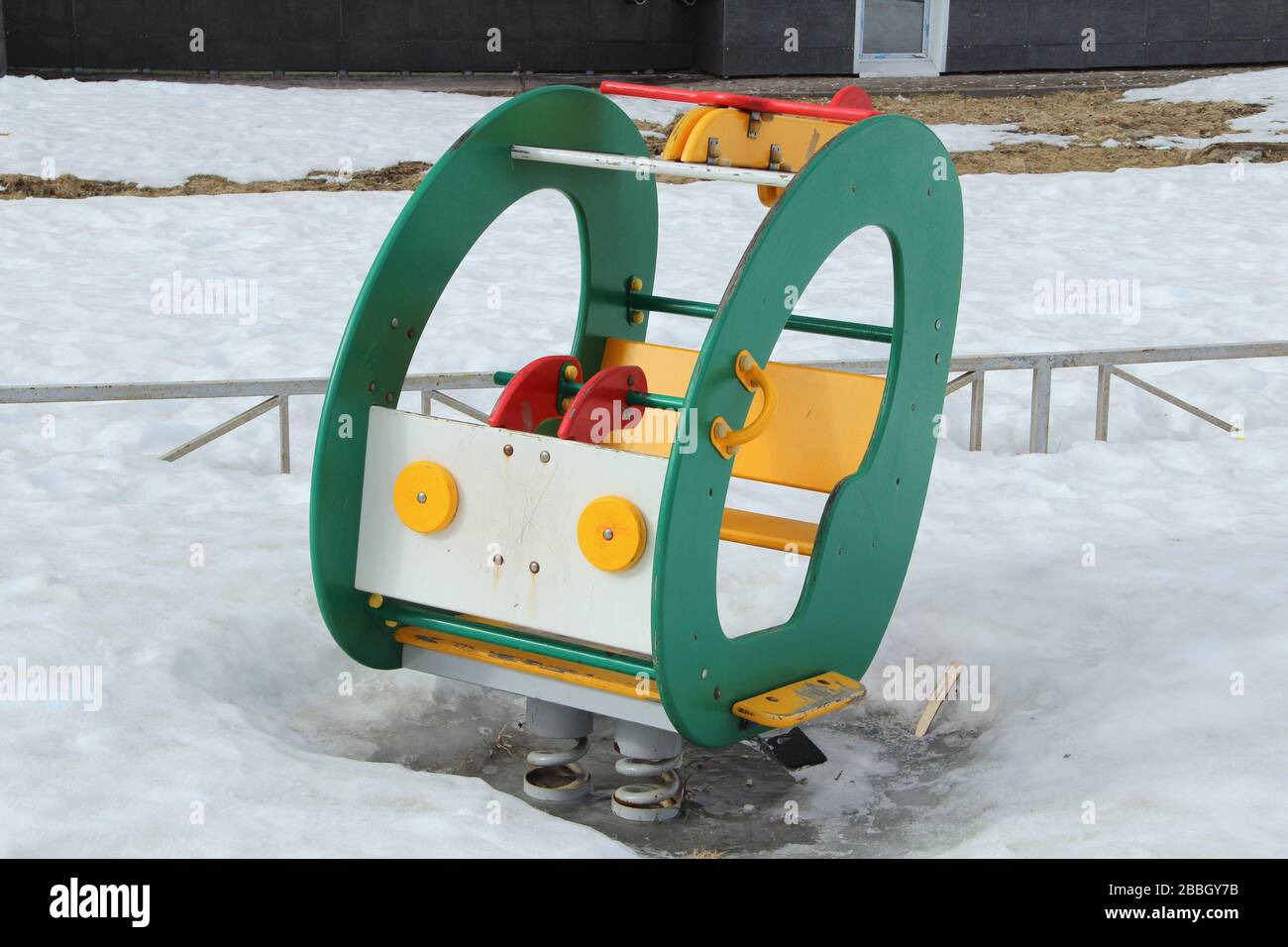Kinderschaukel in Form eines Autos auf dem Spielplatz vor dem Hintergrund winterlicher Schneeverwehungen. Konzept für Kinderunterhaltung und Straßenspiele. Stock-Foto für Web und Druck mit leerem Platz für Text. Stockfoto