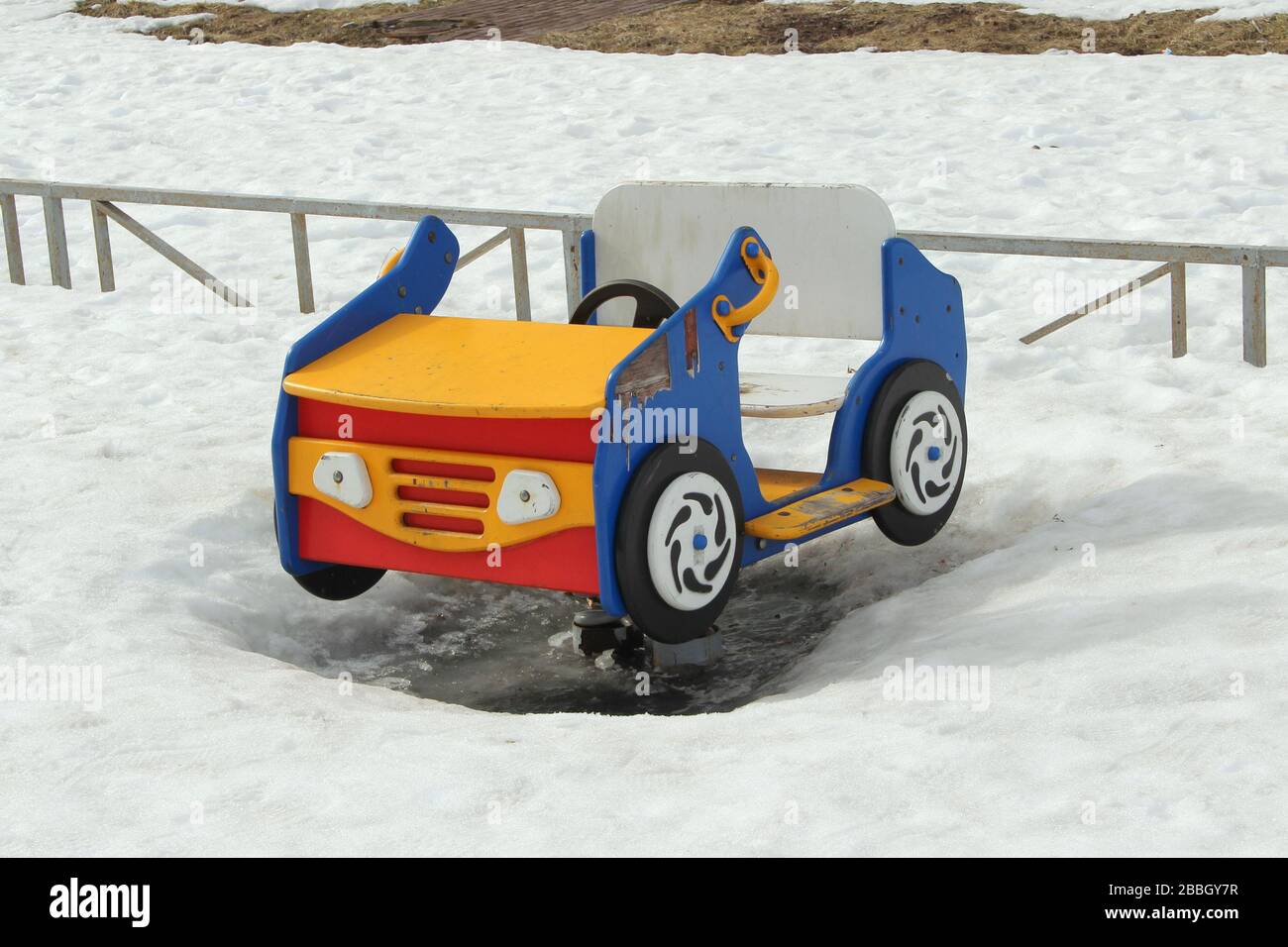 Kinderschaukel in Form eines Autos auf dem Spielplatz vor dem Hintergrund winterlicher Schneeverwehungen. Konzept für Kinderunterhaltung und Straßenspiele. Stock-Foto für Web und Druck mit leerem Platz für Text. Stockfoto
