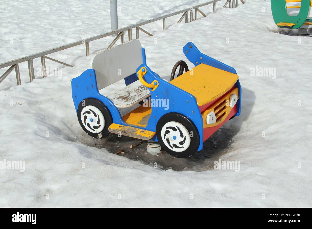 Kinderschaukel in Form eines Autos auf dem Spielplatz vor dem Hintergrund winterlicher Schneeverwehungen. Konzept für Kinderunterhaltung und Straßenspiele. Stock-Foto für Web und Druck mit leerem Platz für Text. Stockfoto