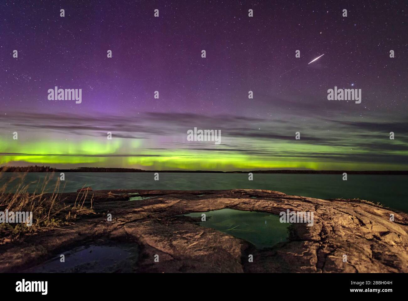Aurora tanzt und ein Meteor streift über den See in Manitoba Kanada großer Felsbrocken in der eastman Region mit Lcouds, die einem schönen Himmel Textur verleihen Stockfoto