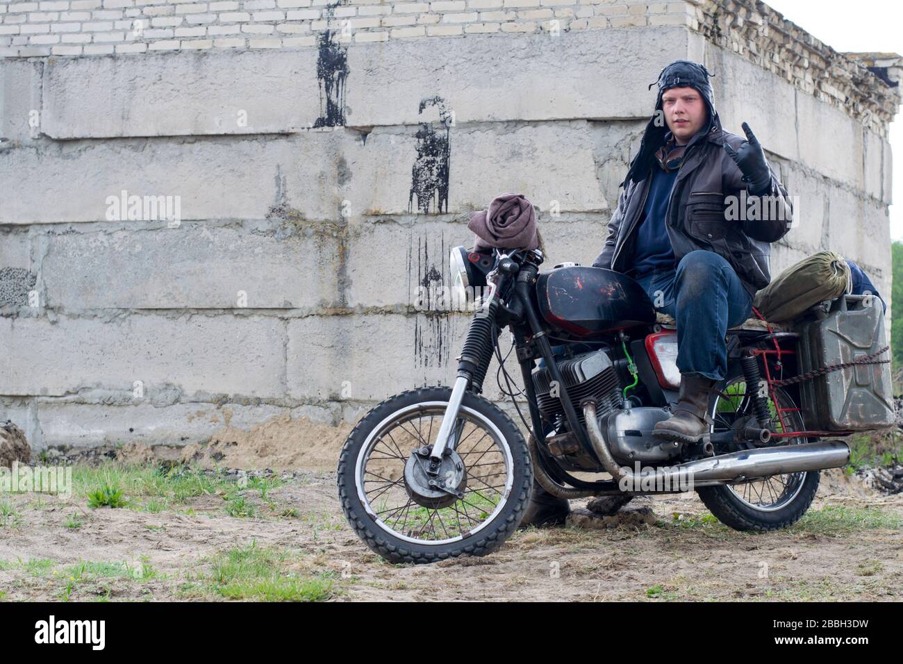 Ein postapokalyptischer Mann auf dem Motorrad in der Nähe des zerstörten Gebäudes Stockfoto