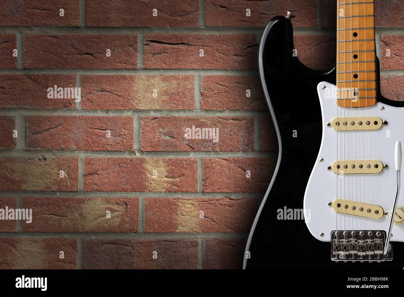 Schwarz-weiße Retro-E-Gitarre auf Backstein-Hintergrund mit Kopierraum Stockfoto