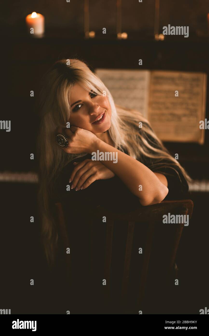 Wunderschönes blondes Mädchen 22-24 Jahre alt, das vor dem Klavier im Zimmer sitzt. Blick auf die Kamera. Stockfoto