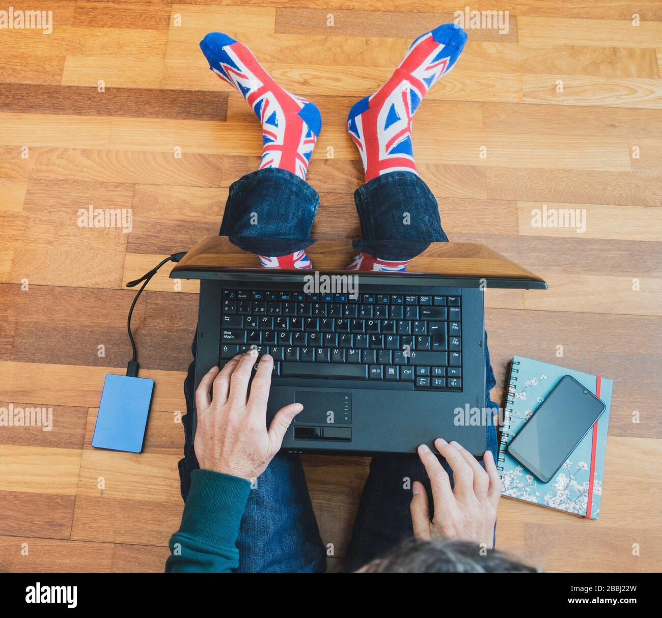 Mann mit union Jack Flag Socke auf Holzboden mit Laptop. Arbeiten von zu Hause, Selbstisolierung, soziale Distanzierung, Coronavirus... Konzept Stockfoto