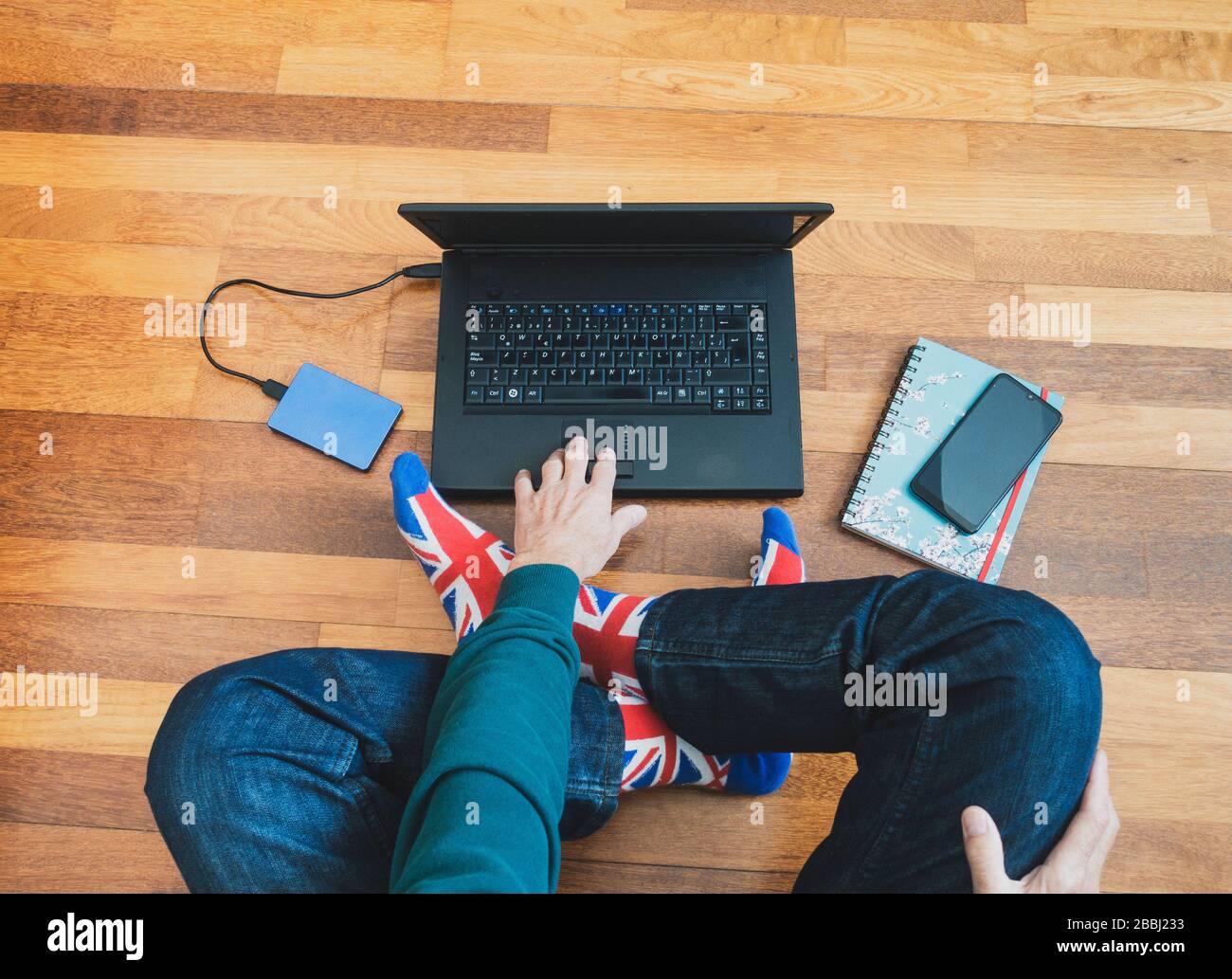 Mann mit union Jack Flag Socke auf Holzboden mit Laptop. Arbeiten von zu Hause, Selbstisolierung, soziale Distanzierung, Coronavirus... Konzept Stockfoto
