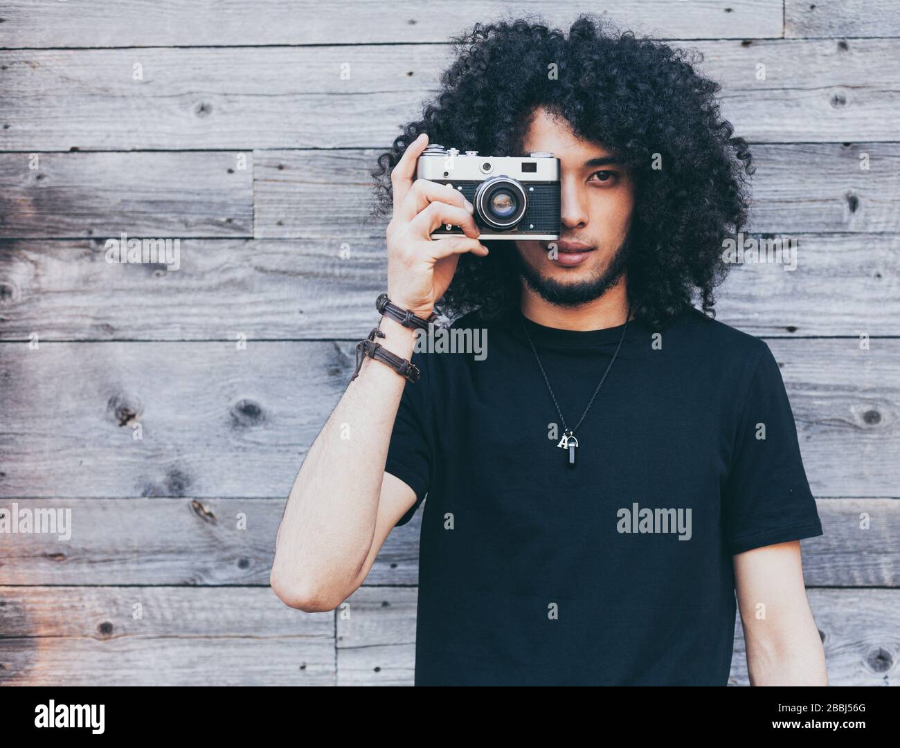 Der afro-typische afro-amerikanische Mann macht sich vor dem Hintergrund alter Bretter ein Bild von einer Vintage-Kamera Stockfoto