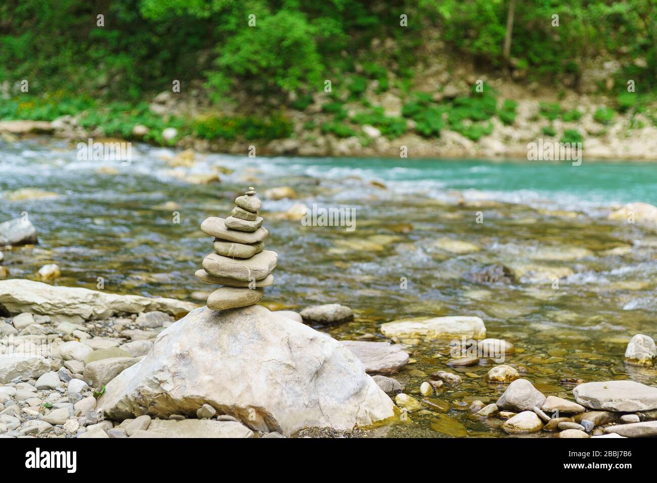 Pyramide aus flachen Steinen am Ufer des schönen Bergflusses Khosta mit türkisfarbenem Wasser in einem Eiben-Box-Hain. Selektiver Fokus Stockfoto