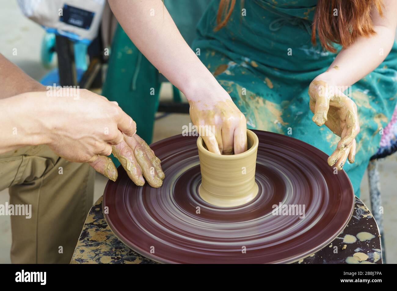 Die Hände eines Meisters und eines Studenten auf einem Potters Rad sculpten einen Pitcher aus Ton. Selektive Fokussierung auf die Hände Stockfoto