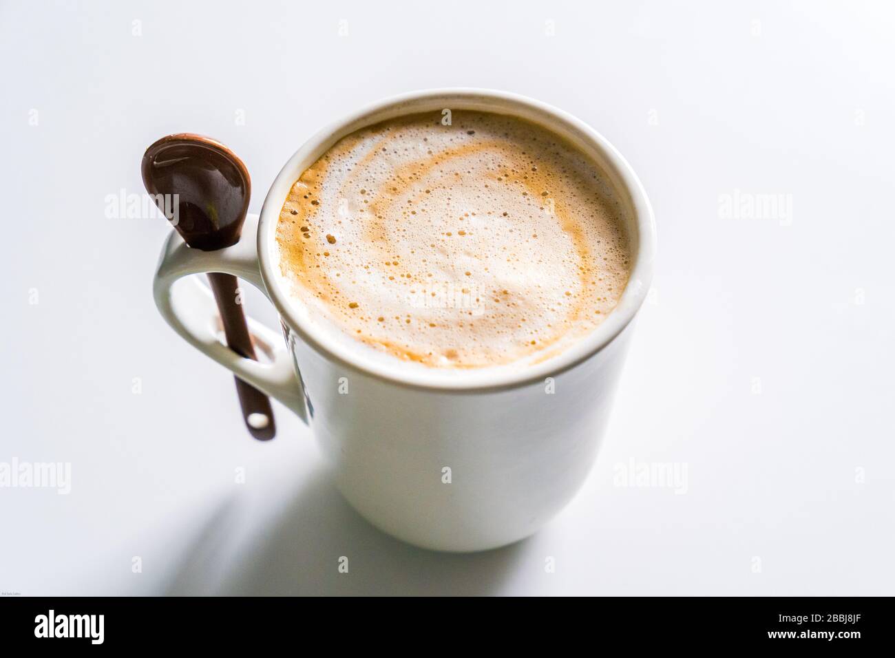 Cremiger Kaffee mit Milch in einer weißen Tasse mit einem Löffel. Stockfoto