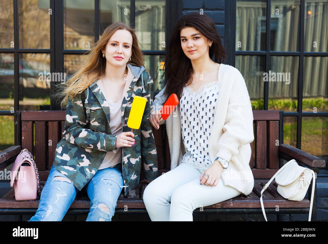 Zwei in Modeoutfits gekleidete Mädchen-Freundinnen ruhen, essen Eis. Eskimo. Stockfoto