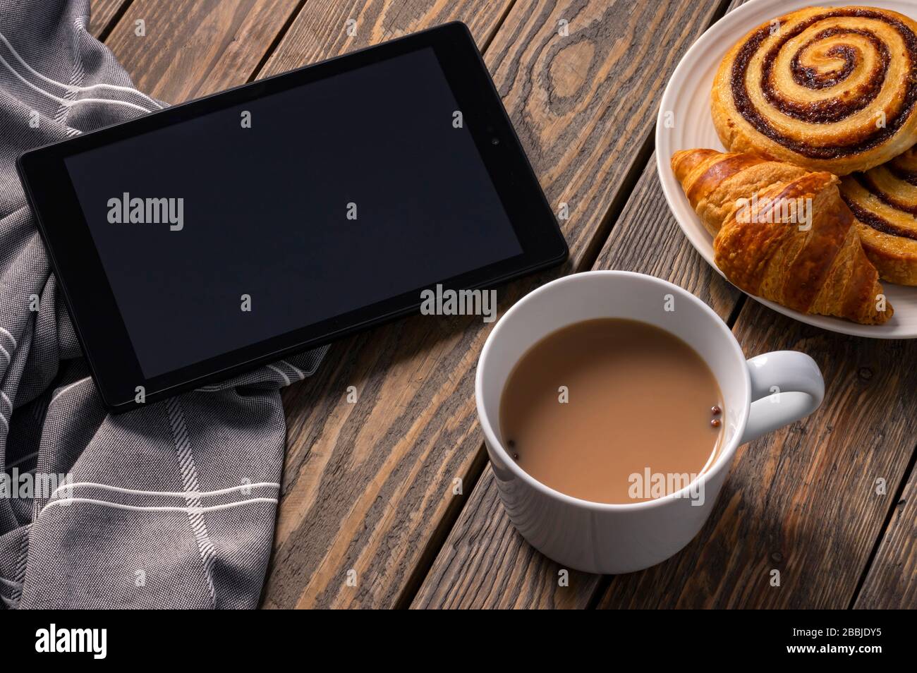 Frühstück auf einem rustikalen Tisch, das neueste auf ihrem elektronischen Gerät beim Tee und Gebäck überprüft. Stockfoto