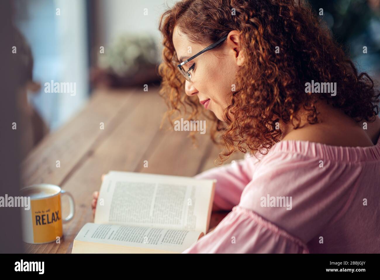 Junge rote Haarfrau mit Brille sitzt und liest ein Buch. Stockfoto