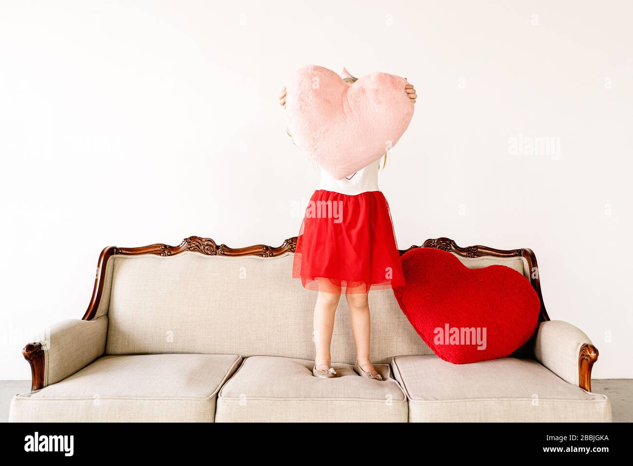 Kleines Mädchen mit großen rosa Herz Kissen auf Couch drinnen Stockfoto