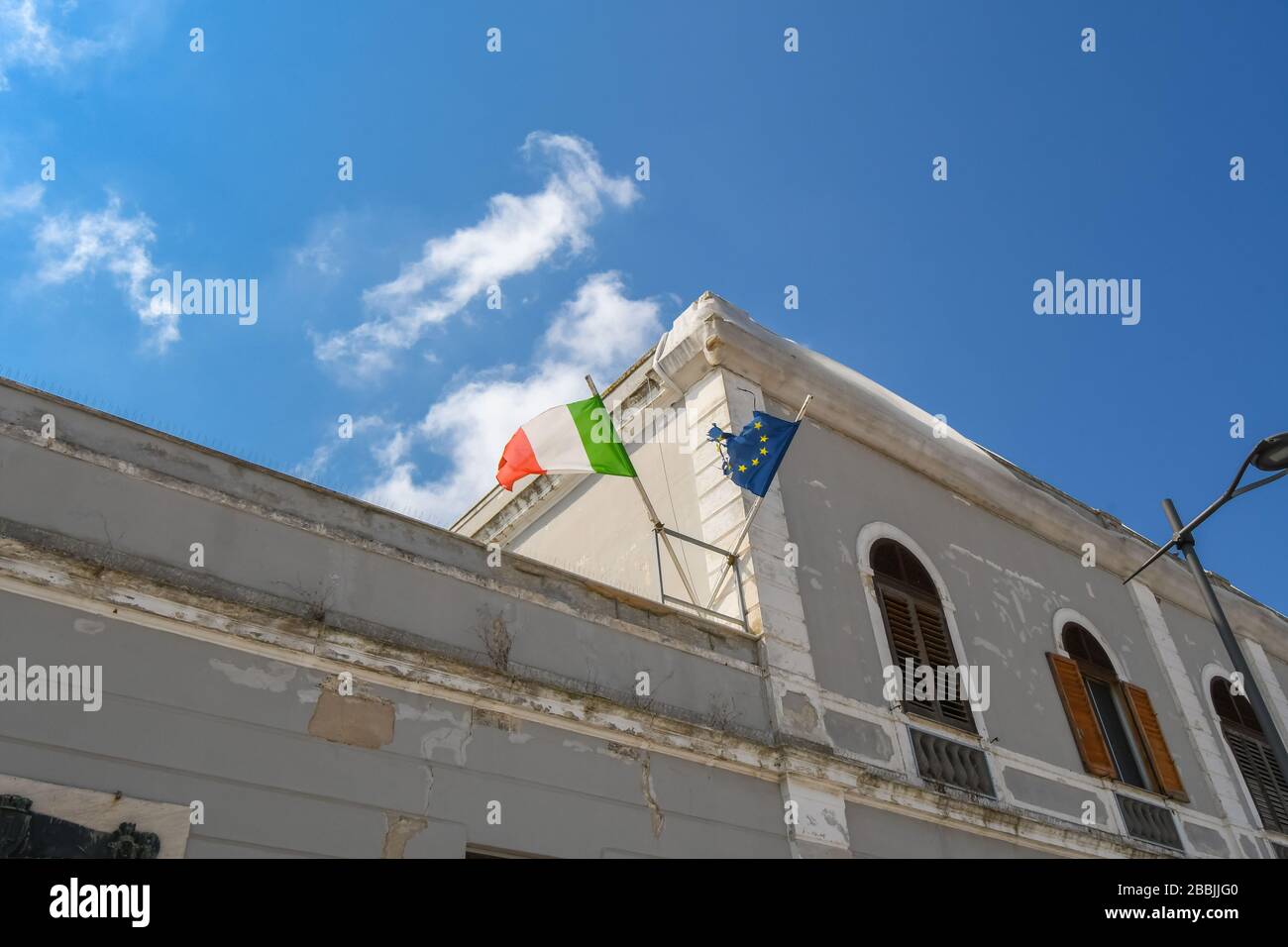 Auf einem abgenutzten Gebäude in Brindisi Italien in der Region Apulien fliegen eine italienische Flagge und eine zerrissene Flagge der Europäischen Union. Stockfoto