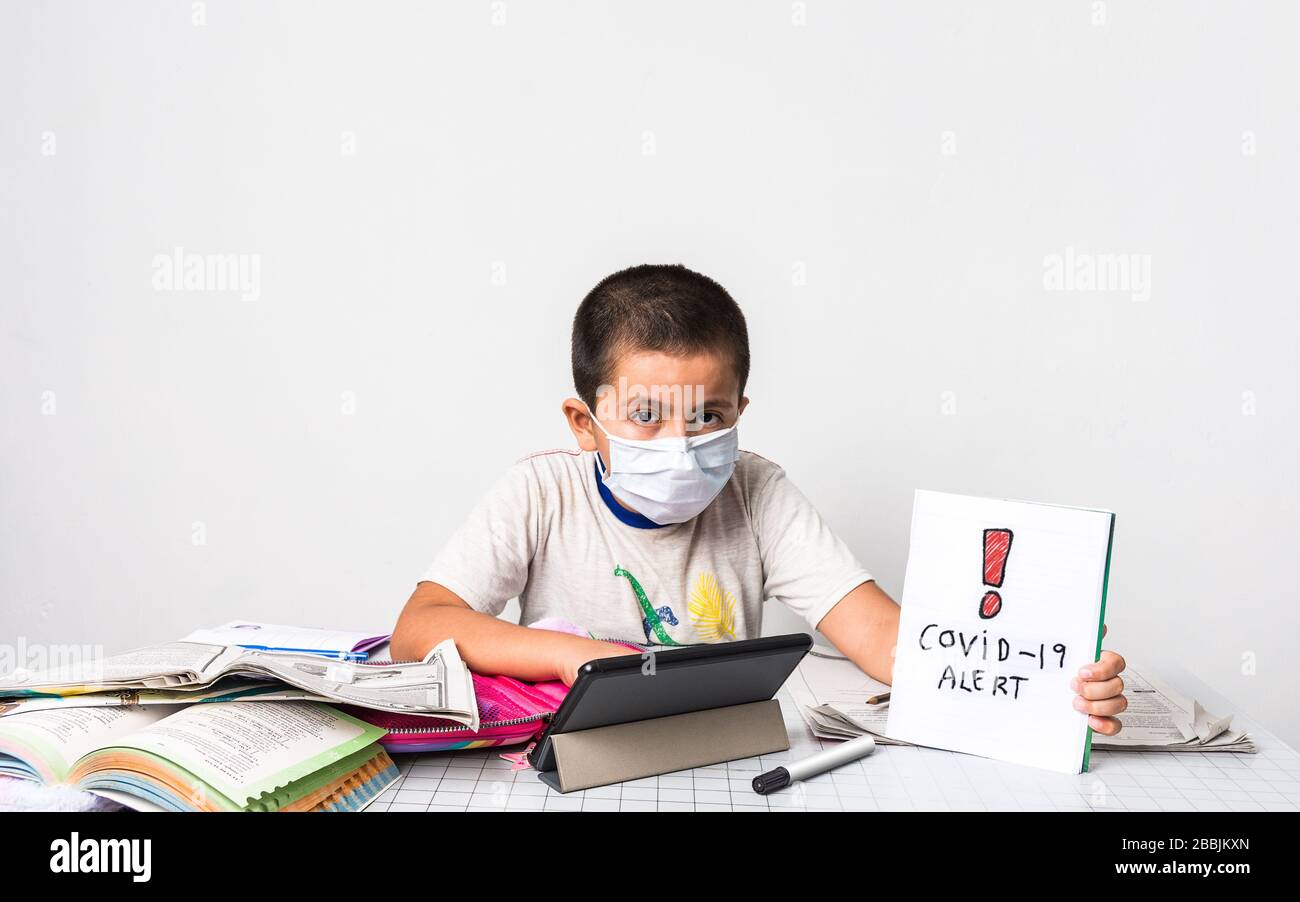 Corona Virus/Home Schooling Konzeptbild mit einem jungen Jungen, der eine Maske trägt, die an einem Tisch sitzt, studieren - Gesundheitswesen und Bildungskonzept Bild Witz Stockfoto