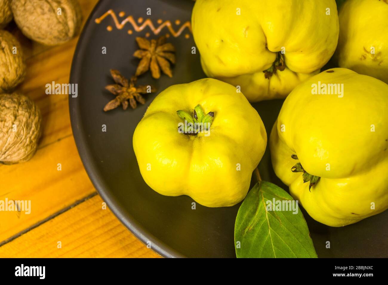Große gelbe Quinzfrüchte auf einer Keramikplatte mit Anis, Zimt und Walnüssen Stockfoto