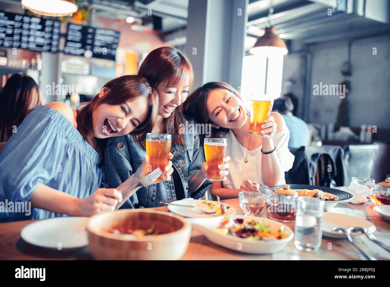 Fröhliche junge Frau, die im Restaurant sitzt und Abendessen und Bier genießen kann Stockfoto