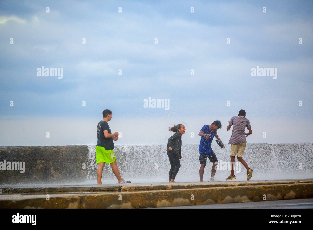 Stürmischer Tag weht Wellen über Malecon, junge Leute, die das Spray erenden, Centro, Havanna, Kuba Stockfoto