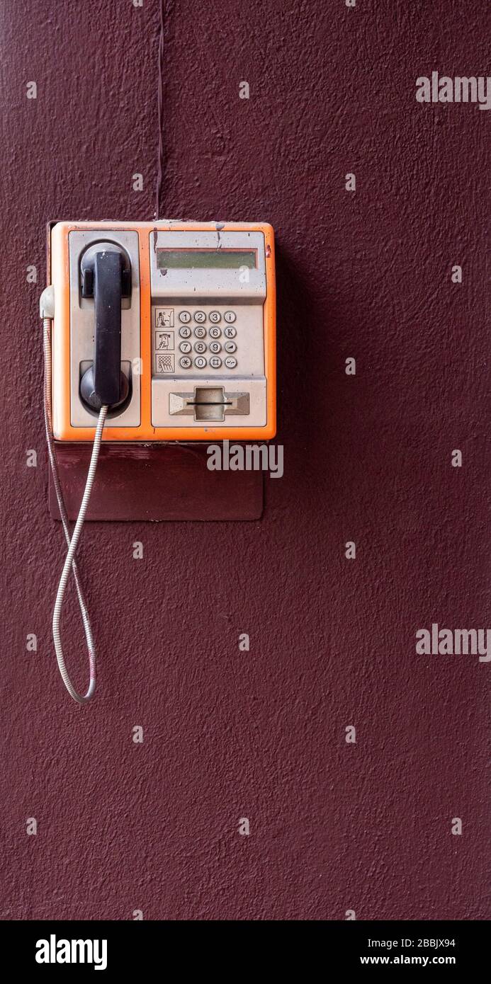 Ein altes öffentliches Telefon, das nur an einer Wand hängt, ohne dass es benutzt wird, Rest einer vergangenen Ära. Stockfoto