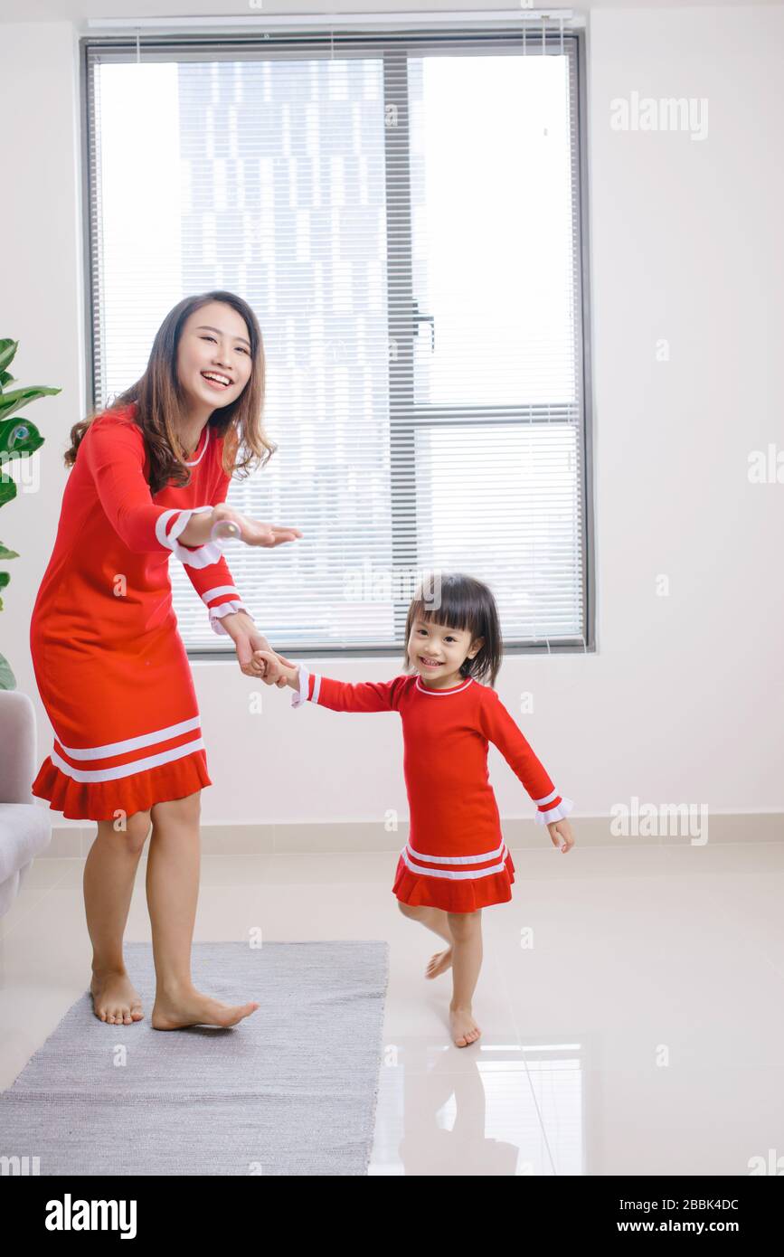 Fröhliche Mutter kleine Tochter, die zu Hause im Wohnzimmer steht und gemeinsam zum Lieblingslied tanzt. Stockfoto