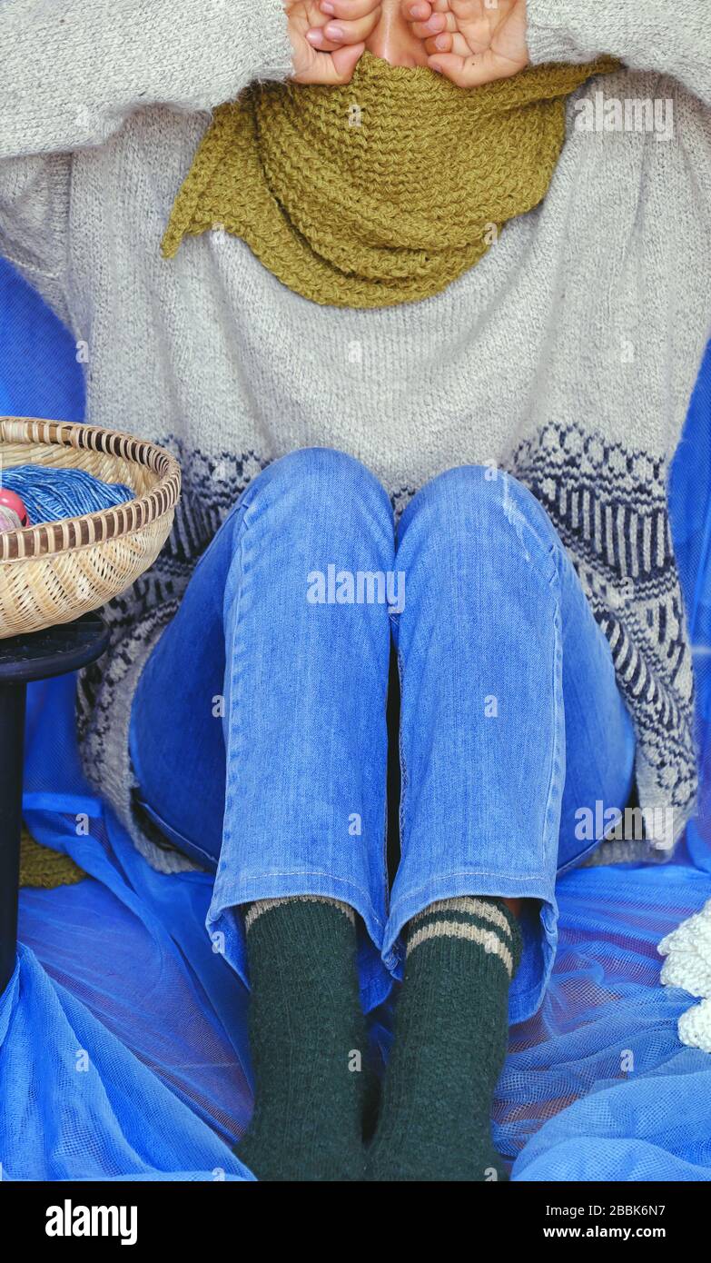 Frau trägt blaue Jeans, weißen Wollpullover, Socken- und moosgrünen Wollschal mit blauem Hintergrund, gestricktes handgefertigtes Produkt, das für den Winter warm wird Stockfoto