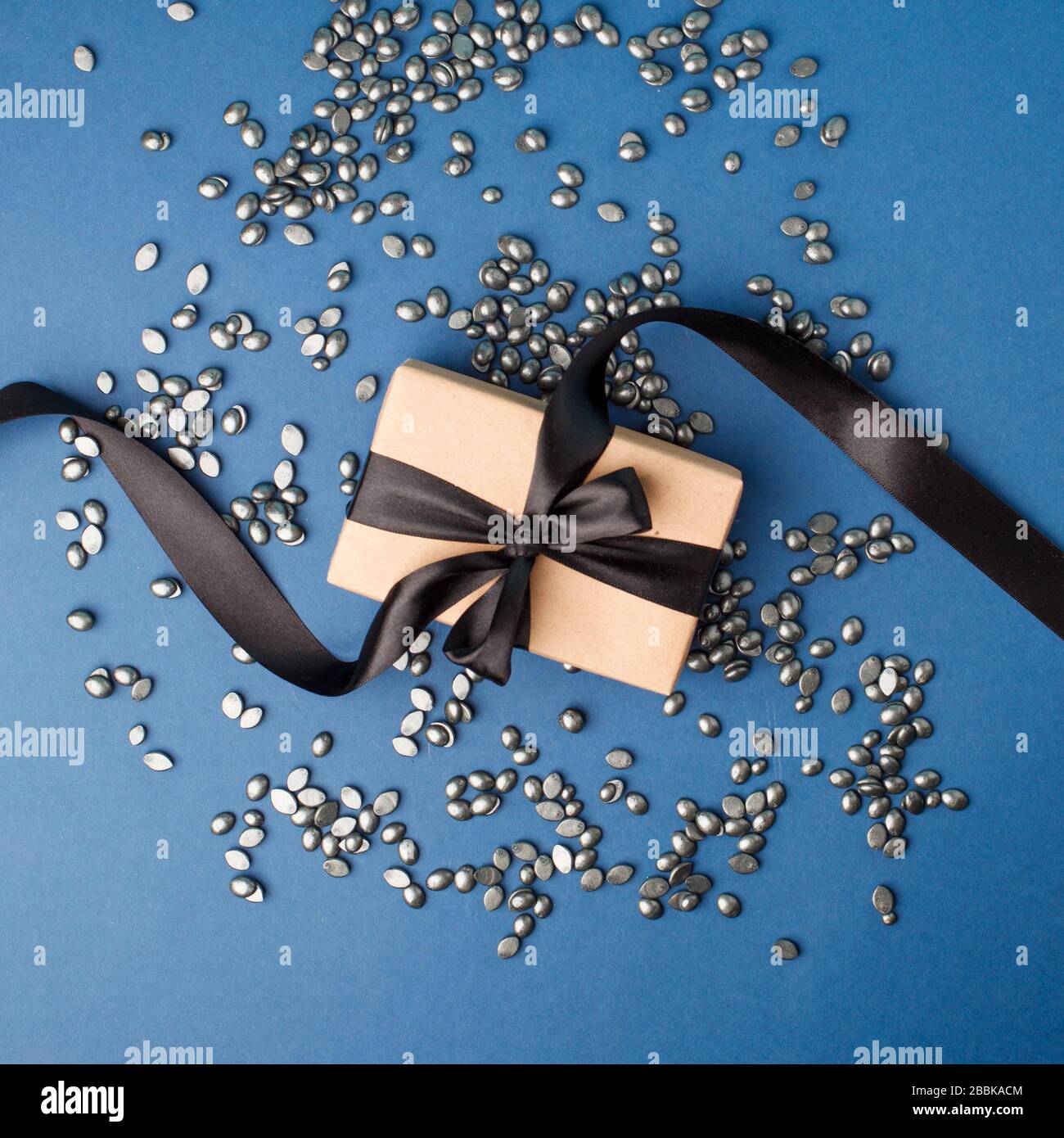 Schwarzes Perlkornwachs für Depilation auf klassischem blauen Hintergrund mit Geschenkbox. Kopierbereich, Banner, Flyer, Coupon minimale Textur. Das Konzept der Promo Stockfoto