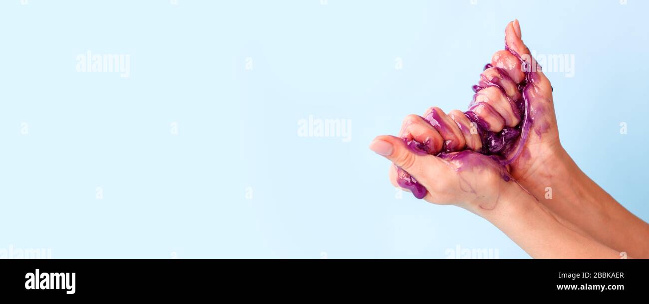 Junge Mädchen Hände mit klebrigem lila Schleim auf blauem Hintergrund, Liqiud Wachs für Depilation, konzeptuelles Flyer Banner mit Copy-Space, Antistress Relax, mo Stockfoto