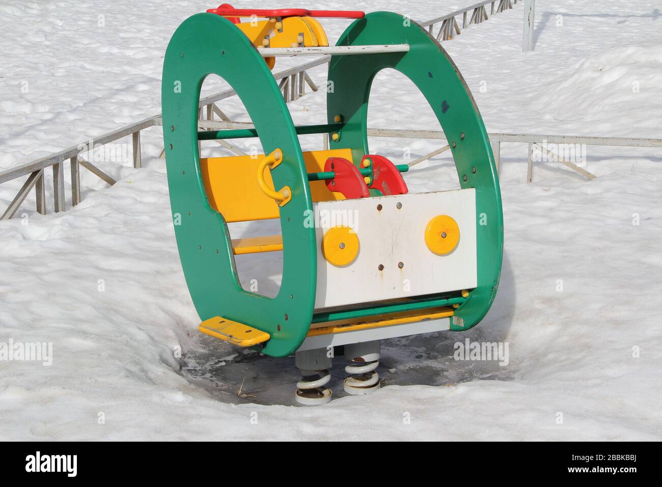 Kinderschaukel in Form eines Autos auf dem Spielplatz vor dem Hintergrund winterlicher Schneeverwehungen. Konzept für Kinderunterhaltung und Straßenspiele. Stock-Foto für Web und Druck mit leerem Platz für Text. Stockfoto