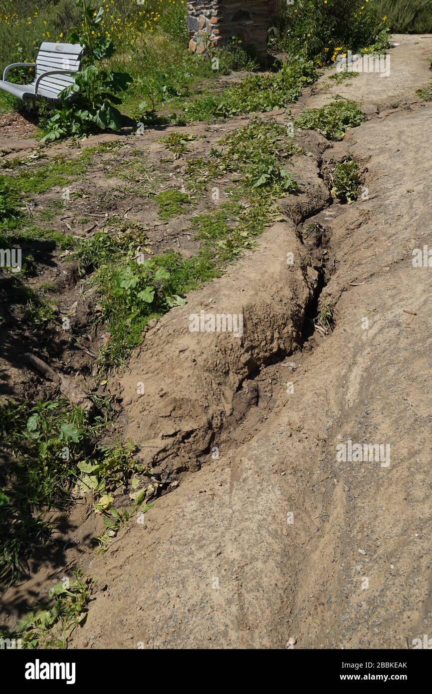 Starke Erosion auf einem öffentlichen Weg durch Sturmabfluss. Es hat sich eine tiefe Wasserrinne gebildet, in der das Wasser, das nicht in die trockene Erde einsinken kann, auf dem Hügel hinunterlief. Stockfoto