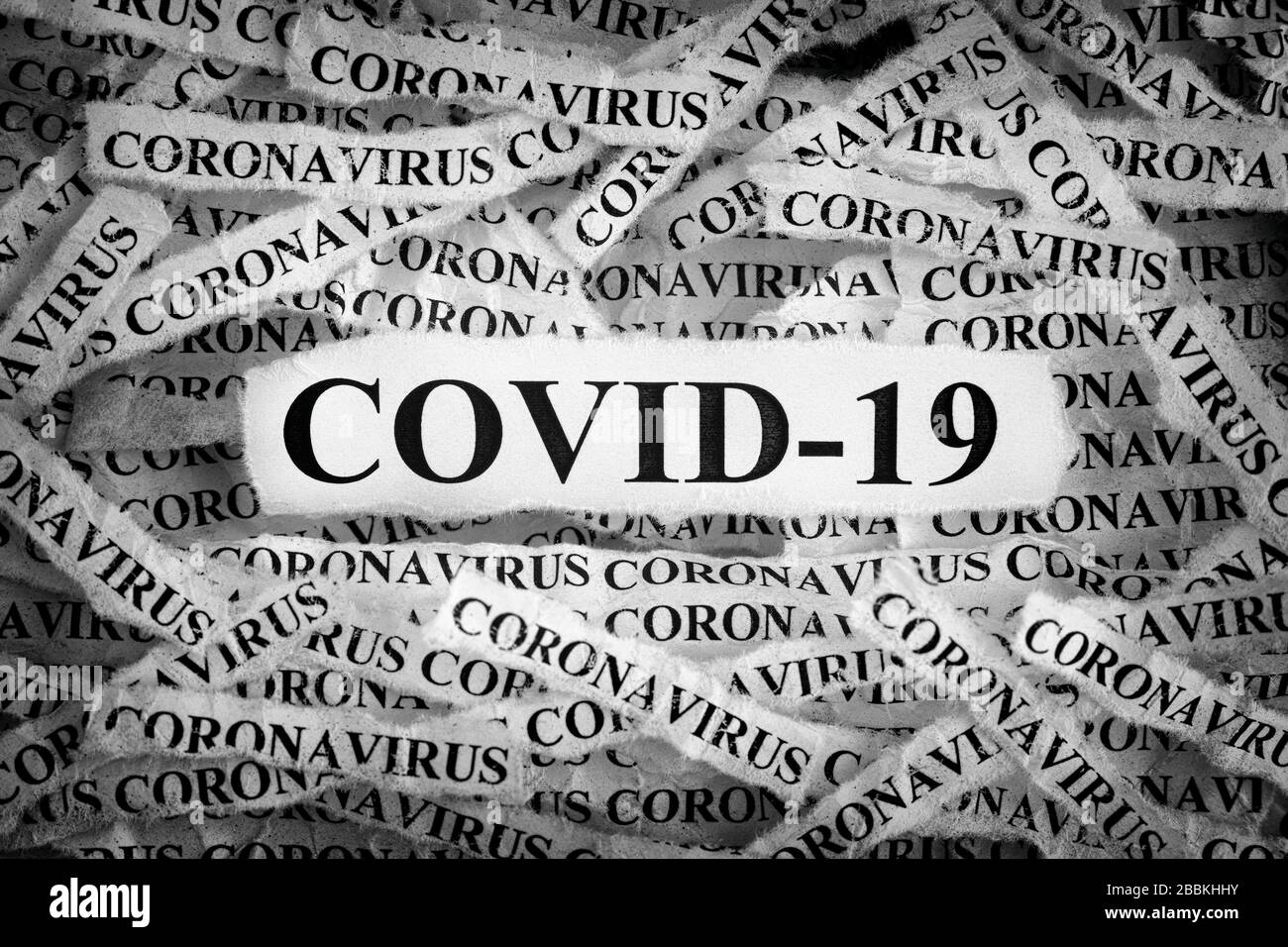 Streifen der Zeitung mit den Wörtern COVID-19 und Coronavirus tippten auf sie. Schwarzweiß. Nahaufnahme. Stockfoto