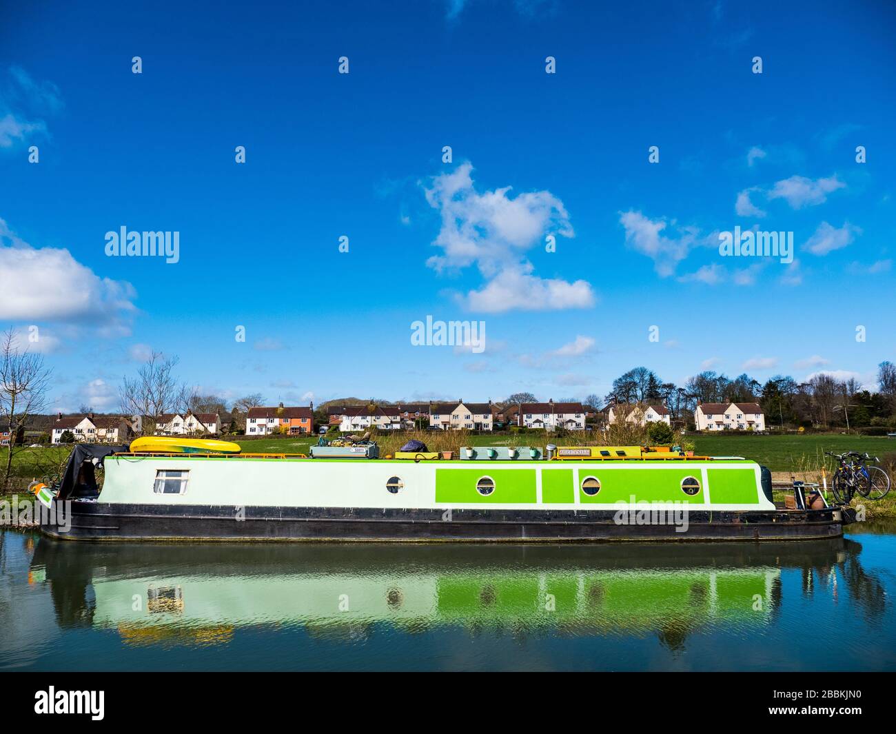 Grünes Narrowboat spiegelt sich auf dem Kennet und Avon Canal, Great Bedwyn, North Wessex Downs, Wiltshire, England, Großbritannien, GB. Stockfoto