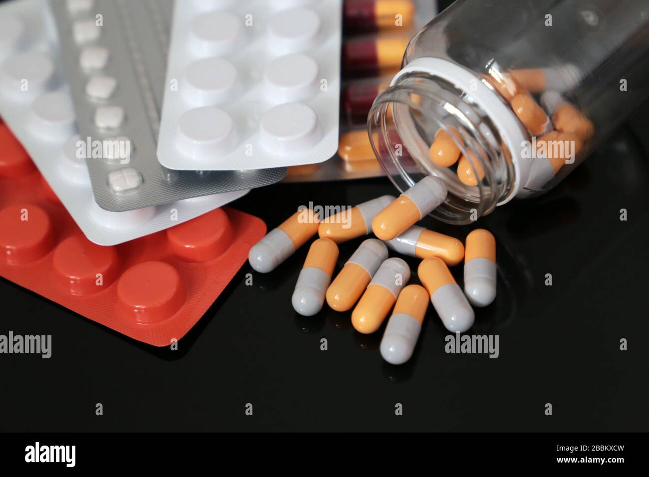 Pillen auf einem dunklen Glastisch, Medikamente in Tabletten und Kapseln, die aus einer Flasche verstreut sind. Konzept des Schutzes von Coronavirus, Apotheke, Antibiotika Stockfoto