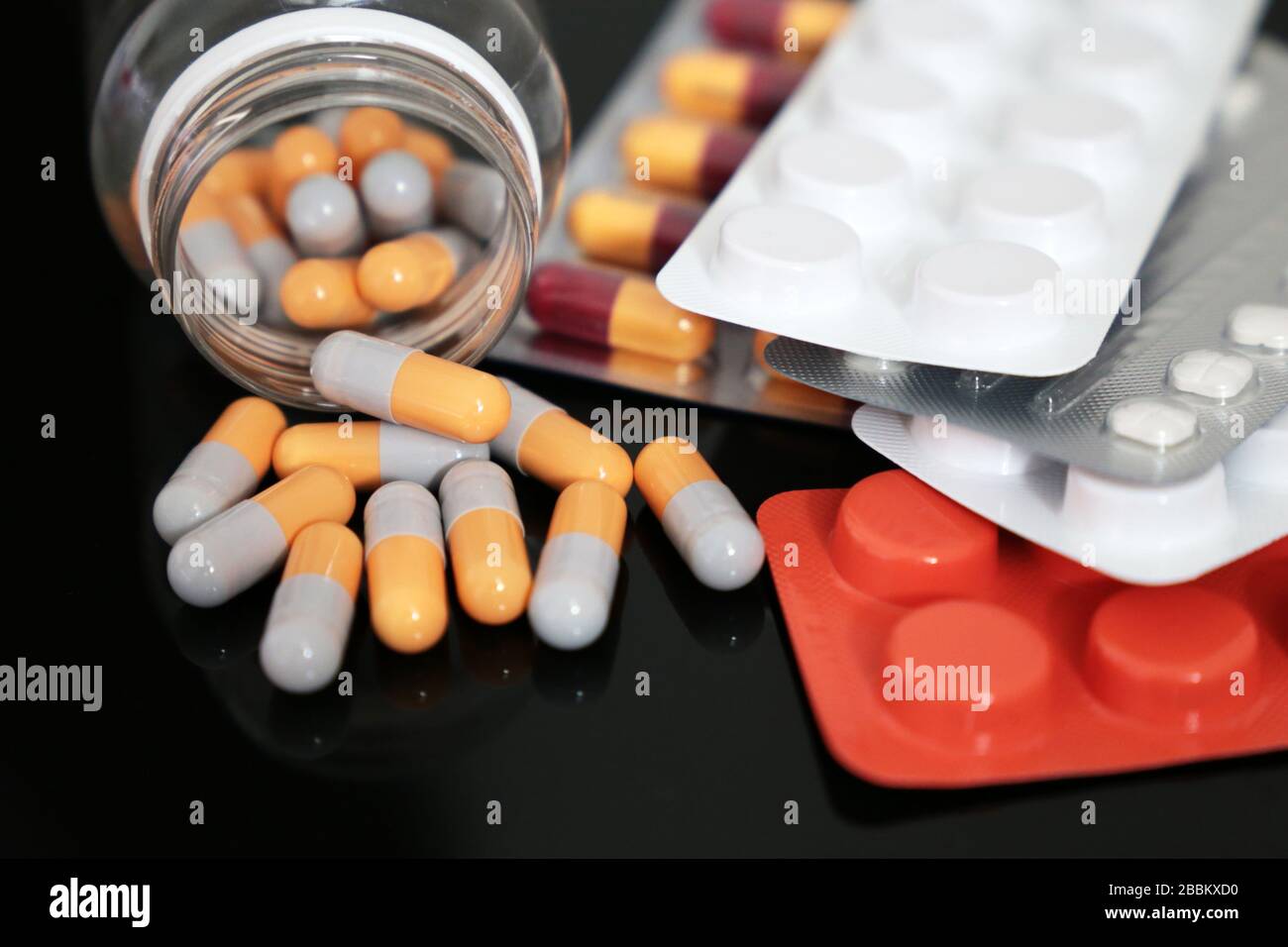 Pillen auf einem dunklen Glastisch, Medikamente in Tabletten und Kapseln, die aus einer Flasche verstreut sind. Konzept des Schutzes von Coronavirus, Apotheke, Antibiotika Stockfoto