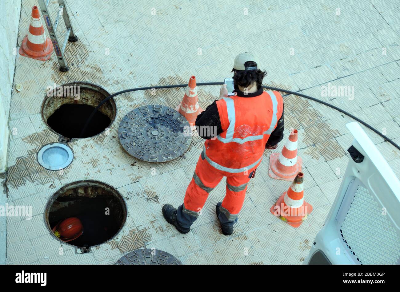 Ein Kanalisationsarbeiter mit nicht abgedeckten Mannlochabdeckungen oder Ablaufabdeckungen bereitet sich auf Arbeiten an unterirdischen Abwasserkanälen, Abflüssen oder Abflussarbeiten vor Stockfoto