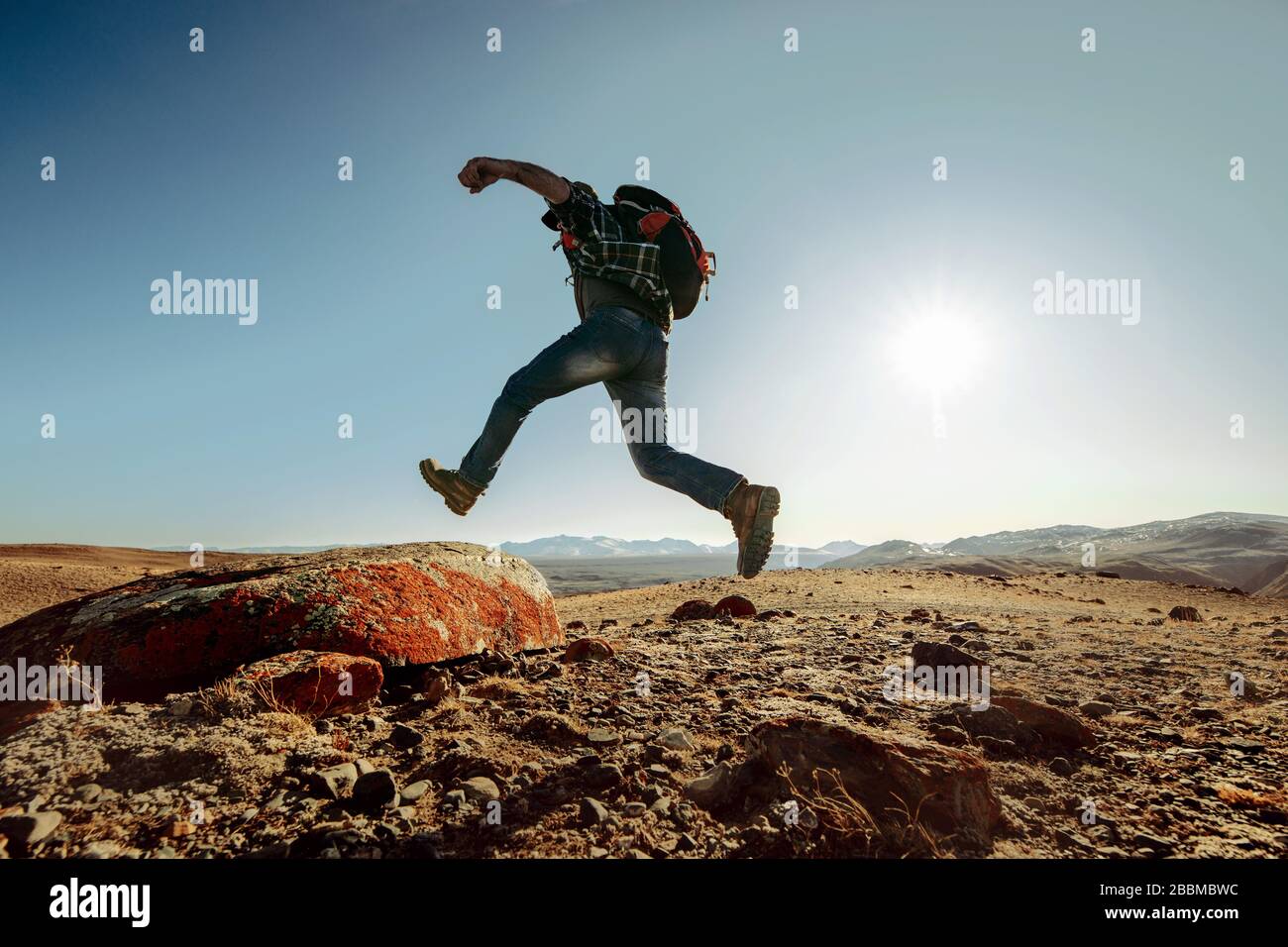 Wanderer oder Reisender mit Rucksack springt auf großen Felsen gegen blauen Himmel bei Sonnenuntergang Stockfoto