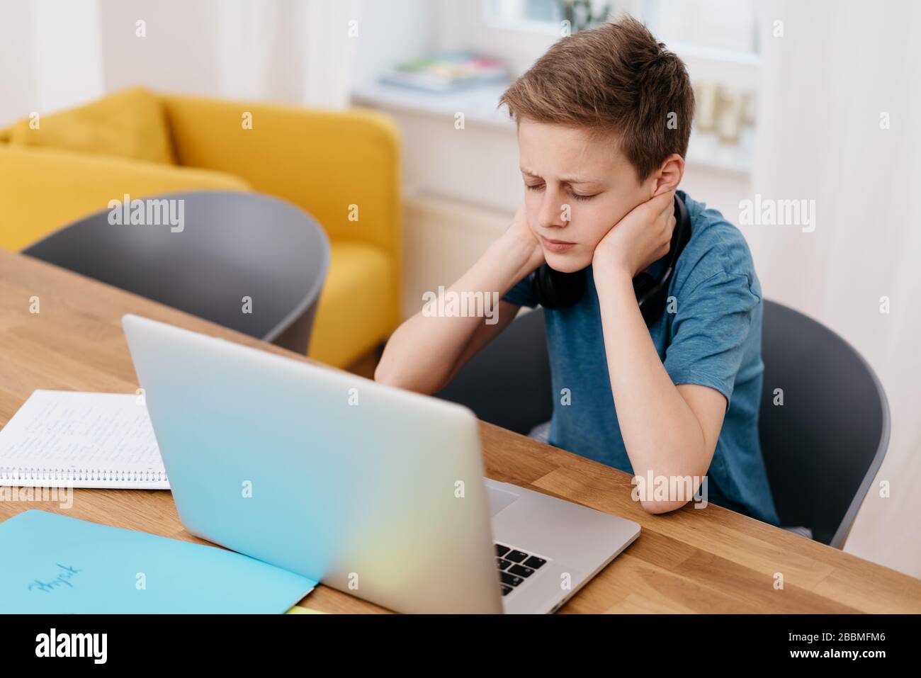 Der junge Junge, der sich auf sein E-Learning konzentriert, während er von zu Hause aus während des Covid-19-Lockdown-Sitzens auf einem Laptop arbeitet Stockfoto