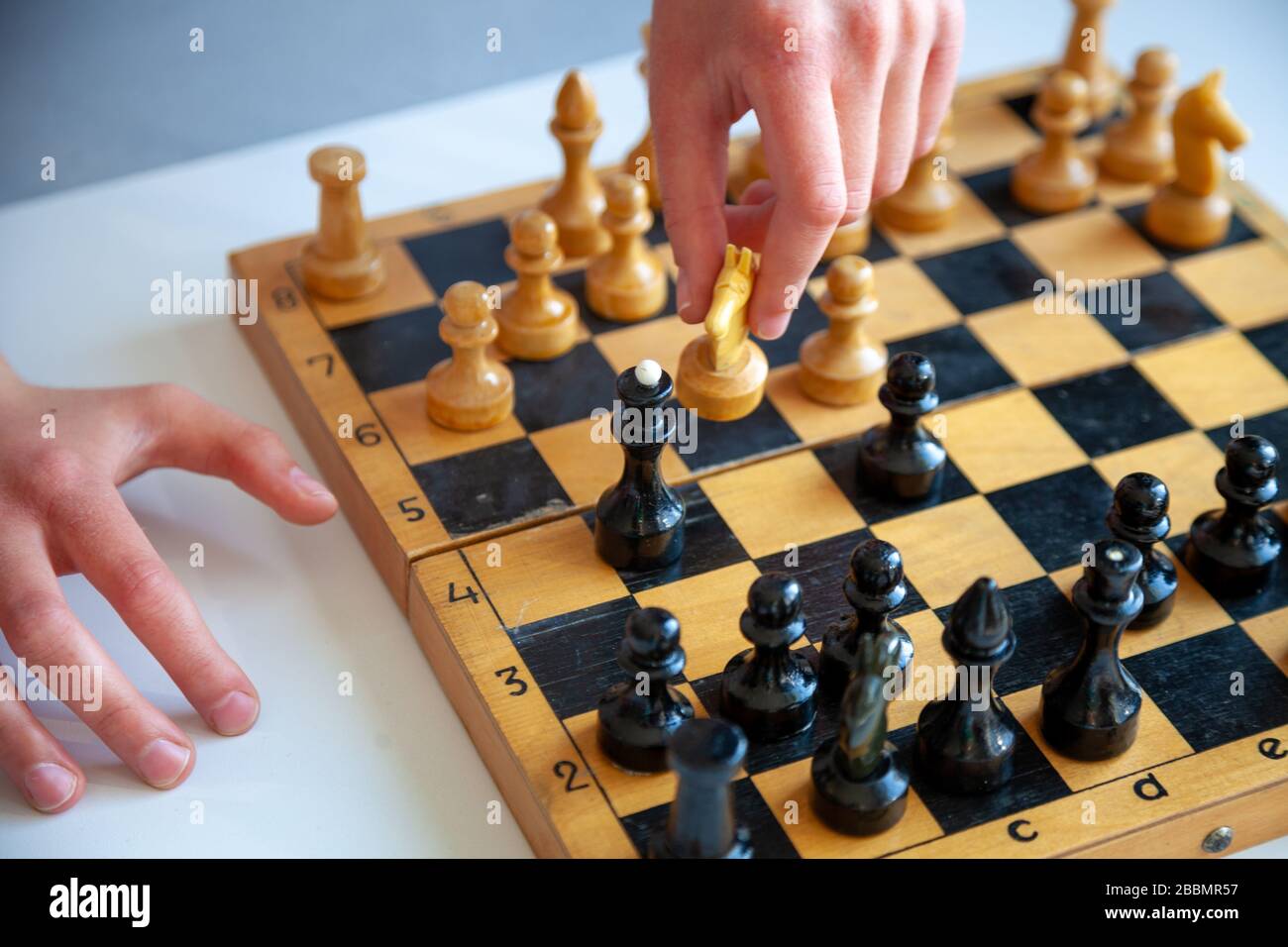 Ein Kind spielt allein Schach. Altes Holzkesselbrett. Kinderhände. Schachfiguren auf einem Schachbrett. Stockfoto