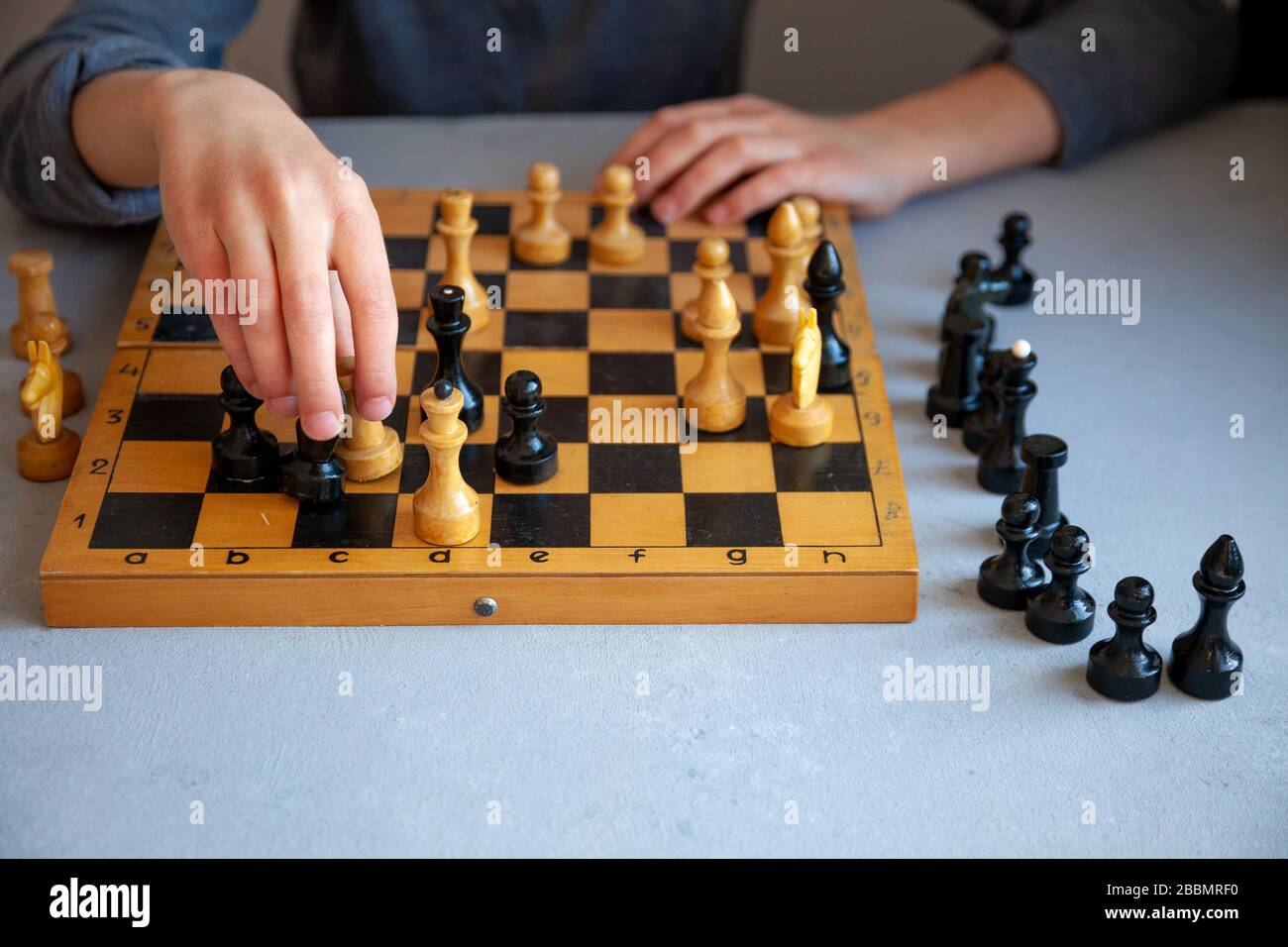 Ein Kind spielt allein Schach. Altes Holzkesselbrett. Kinderhände. Schachfiguren auf einem Schachbrett. Stockfoto