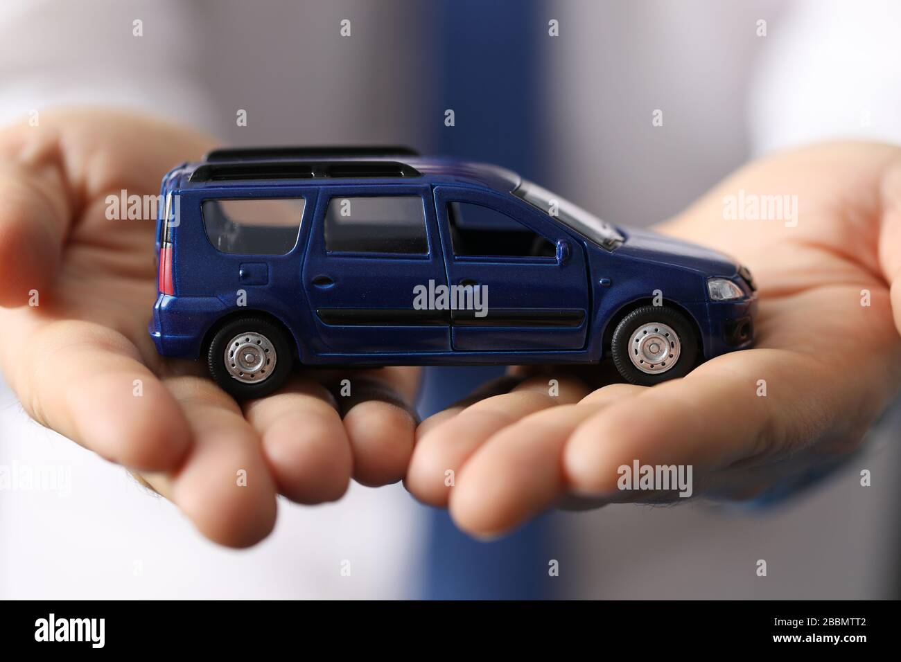 In der Nähe hält der Mann im Hemd ein blaues Minivan-Auto für Spielzeug Stockfoto