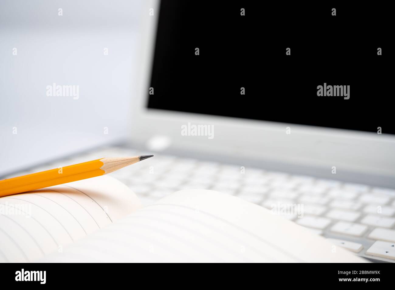 Online-Lernkonzept. Auf der Tastatur des Laptops befinden sich ein gefüttertes Notebook und ein gelber Bleistift. Stockfoto