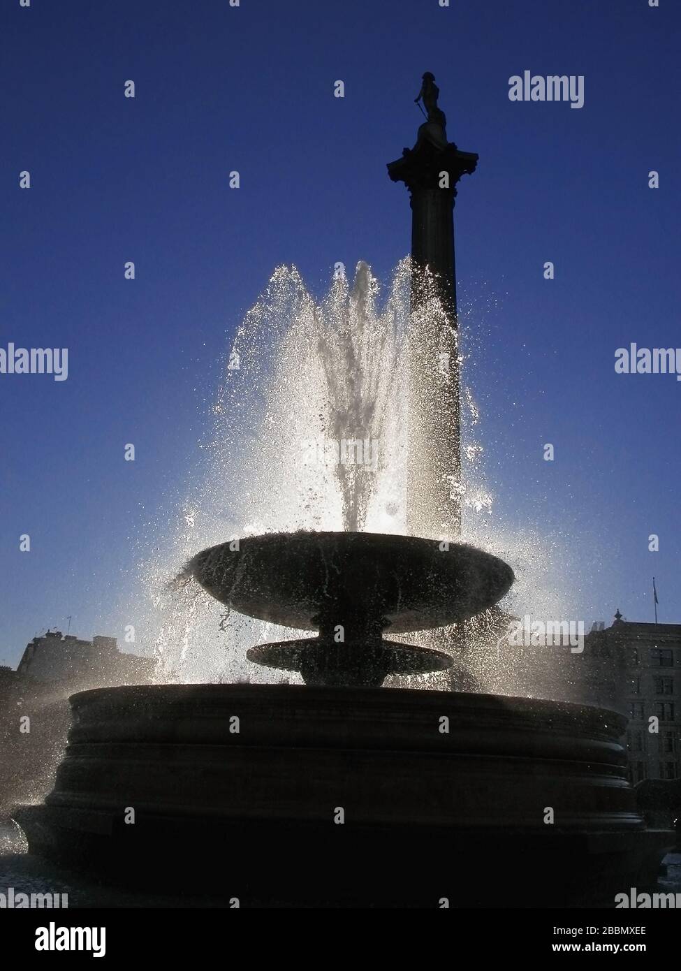 Nelsons Säule und Springbrunnen, Trafalgar Square, London, England, Großbritannien: Silhouette und sonniger Wasserstrahl mit Hintergrundbeleuchtung Stockfoto