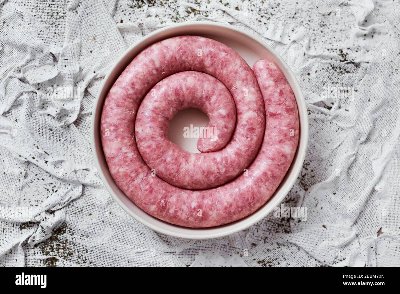 Hochwinkeliger Blick auf eine gerollte Botifarra, eine für Katalonien typische Schweinefleischwurst in Spanien, auf einem Teller, auf einem weißen texturierten Textilhintergrund Stockfoto