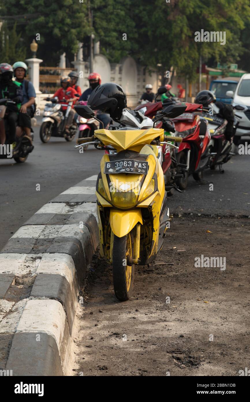 Jakarta, Indonesien - 13. Juli 2019: Ein gelbes, waspenähnliches Motorroller-Motorrad steht auf einer Straße in Jakarta, während der Verkehr weiter geht. Stockfoto