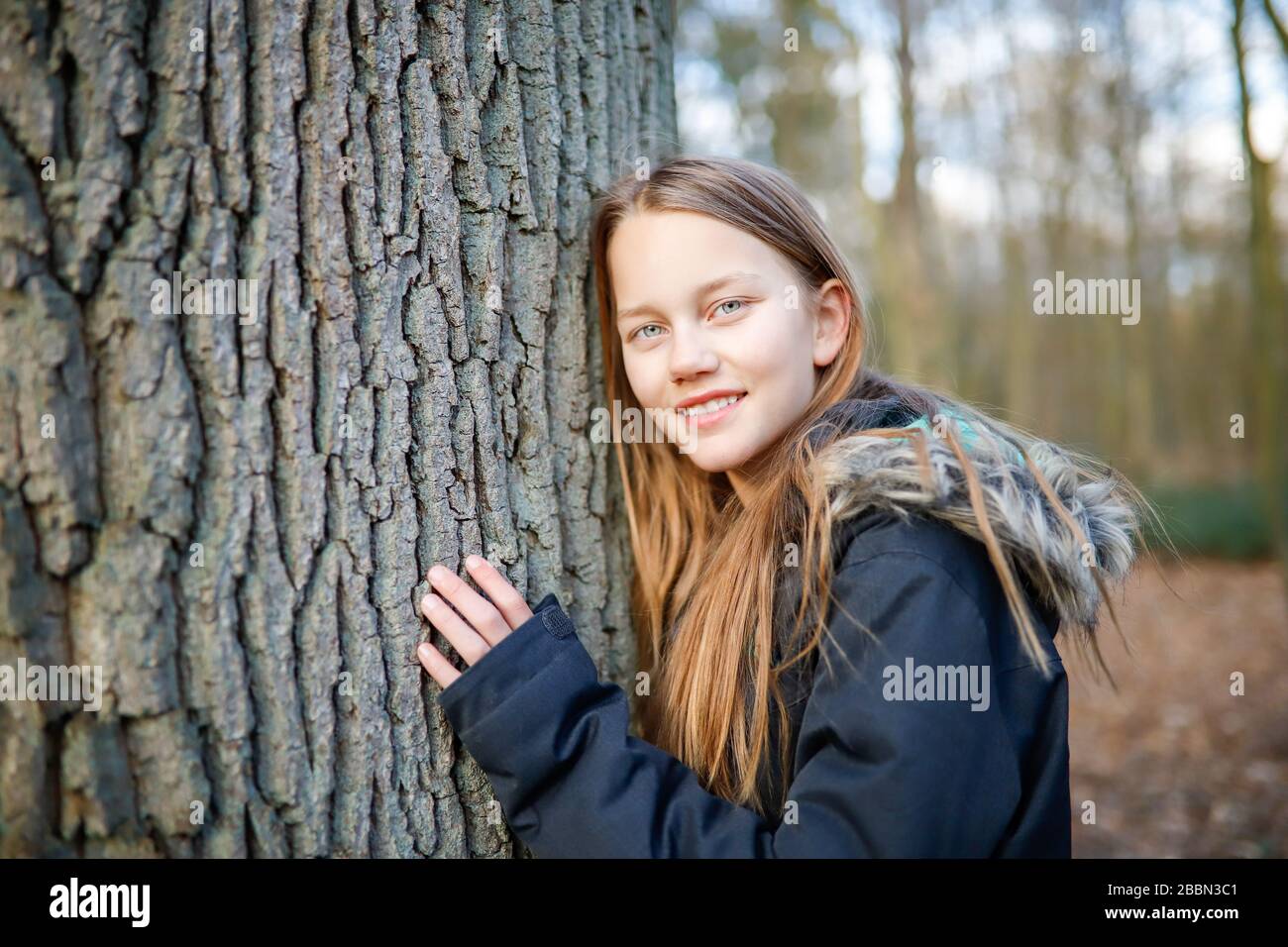 Ein 11 Jahre altes Mädchen lehnt sich an den Stamm eines riesigen Baumes Stockfoto