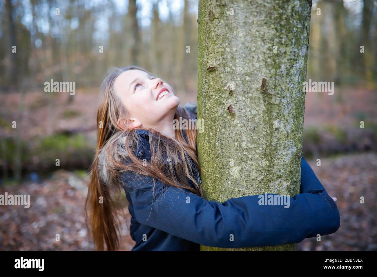 Ein 11 Jahre altes Mädchen umarmt den Stamm eines kleinen Baumes Stockfoto
